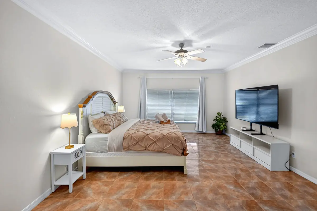 Primary bedroom with a large bed, TV and ceiling fan